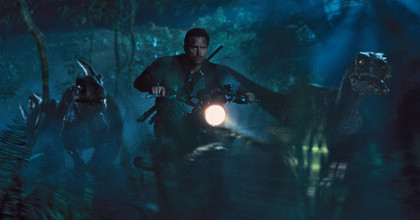 Movie still of Chris Pratt riding a motorcycle, leading a pack of velociraptors