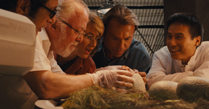 Still from Jurassic Park showing all the scientists huddled around a hatching dinosaur.