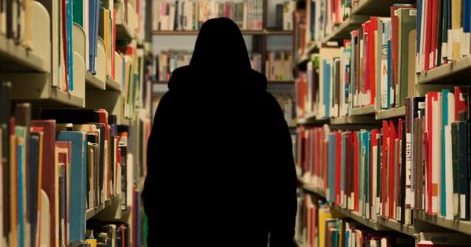 Photo of an aisle between two book shelves with a person's silhouette in the middle