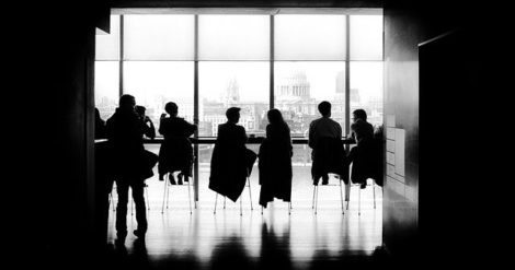 B&W photo of silhouetted people sitting in a circle talking.