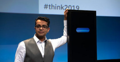 Photo of Harish Natarajan and Project Debater, a black monolith with blue lights