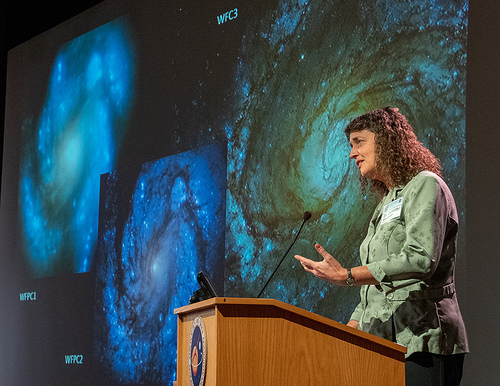 Photo of Jennifer Wiseman lecturing in front of galaxy images.