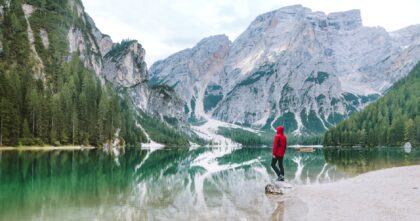 man wearing red hoodie standing near body of water with view of mountains